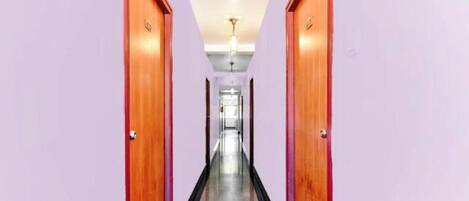 Un pasillo con puertas de madera a ambos lados, que conduce a una habitación luminosa con una lámpara en el techo.