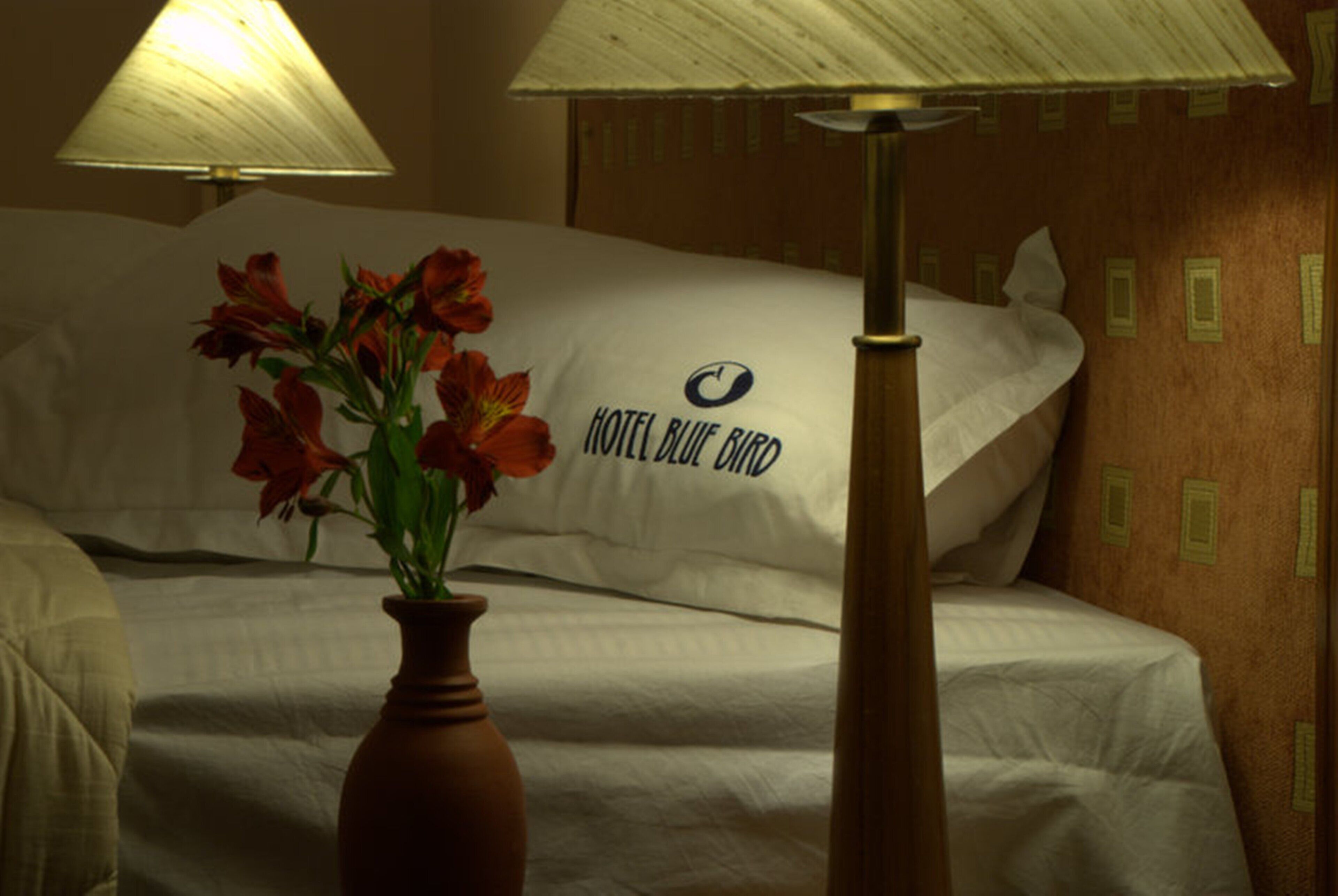 Ein Hotelzimmer mit Bett, Blumen in einer Vase und einer Lampe.
