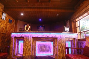 Una habitación con techo de madera, pared de piedra iluminada con luz púrpura, un certificado enmarcado y una ventana con vistas.