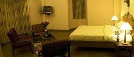 Habitación de hotel con una cama, una silla, una mesita, una lámpara y un televisor en la pared.