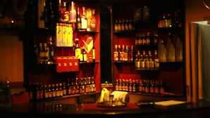 A bar area with shelves of bottles and glasses, a counter with a napkin holder, and a decorative item in the center. - Hotel Blue Bird (Ootacamund)