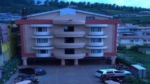 A multi-story building with a central entrance, surrounded by parked cars and motorcycles. - Hotel Blue Bird (Ootacamund)