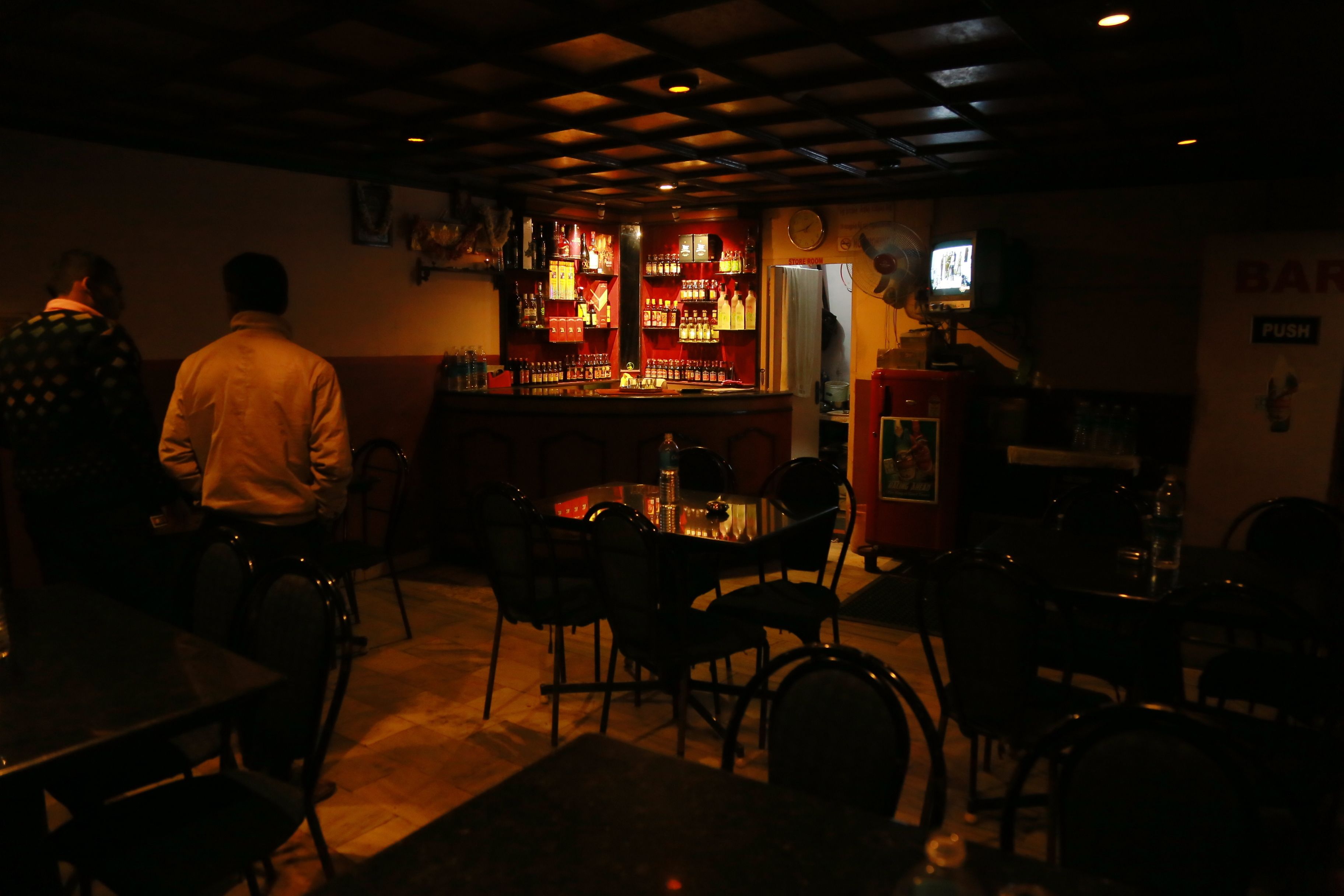 Zona de bar amb poca llum, barra, cadires i televisió.