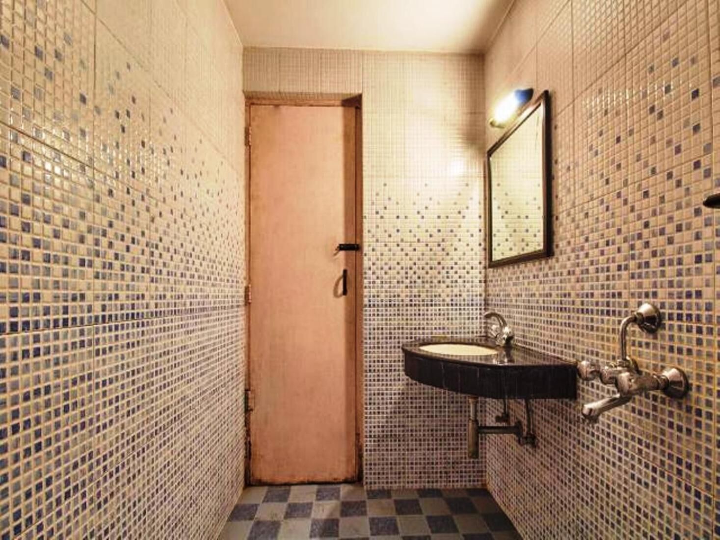A small bathroom with a tiled wall, a sink, a mirror, and a door.