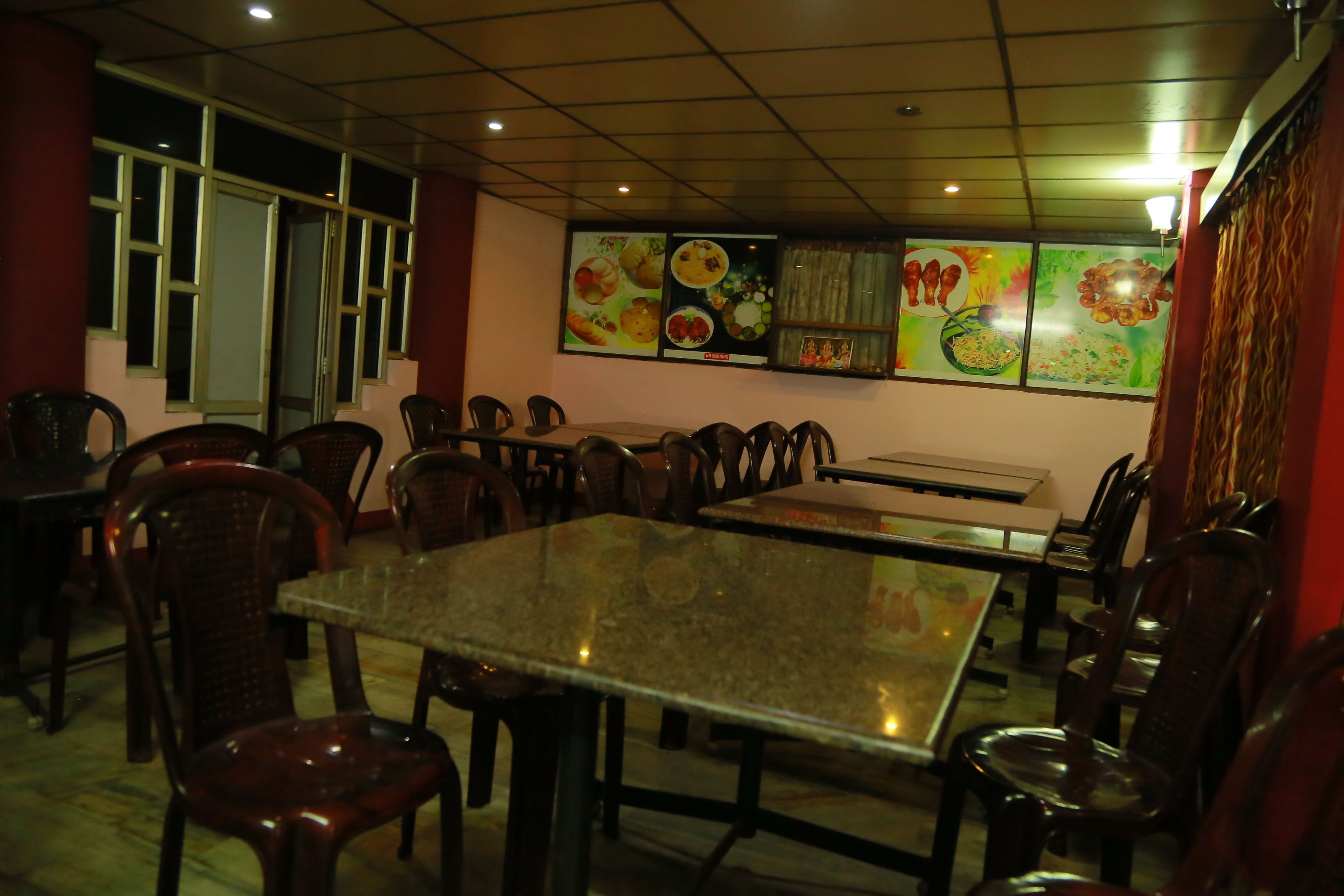 L’intérieur d’un restaurant, avec de nombreuses tables et chaises, un plafond carrelé et des décorations murales représentant des produits alimentaires.