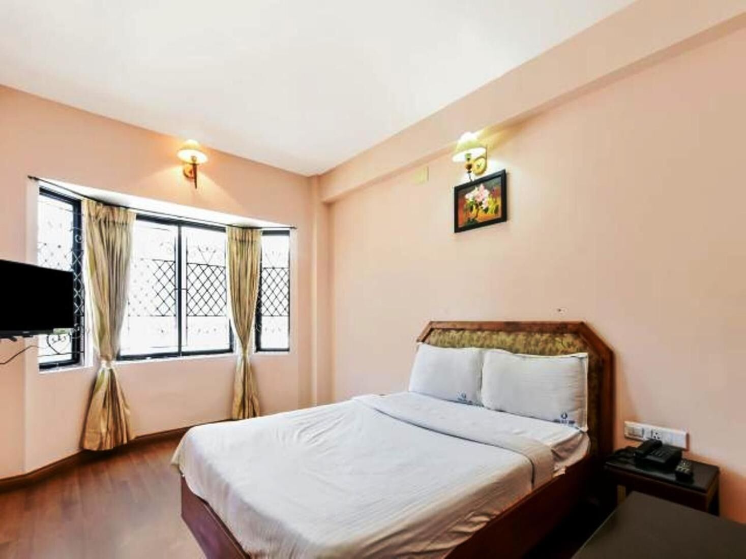 Une chambre à coucher comprenant un lit, une table de chevet, un téléviseur fixé au mur et une fenêtre avec des rideaux.