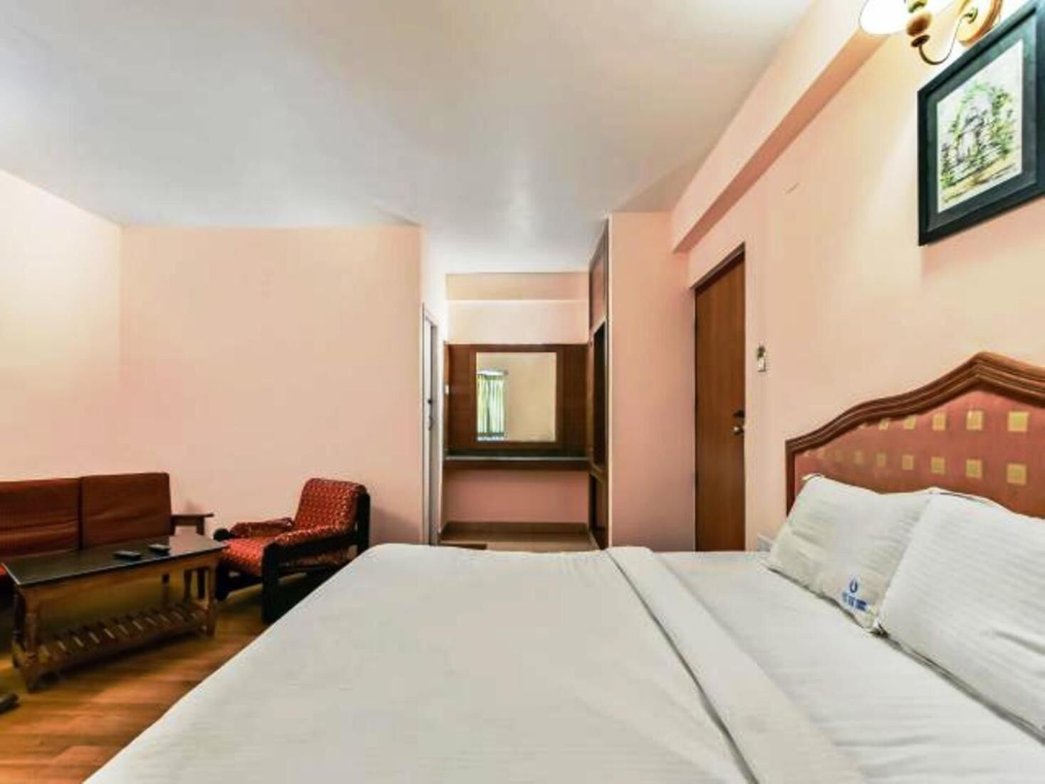 A hotel room with a bed, a wooden bench, a chair, and a mirror.