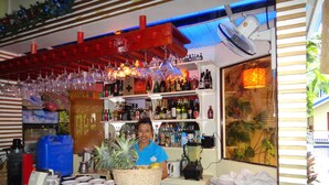 A bar area with shelves of liquor bottles, a fan, and a counter with a basket of fruits. - Blue Lagoon Inn & Suites (Puerto Princesa)