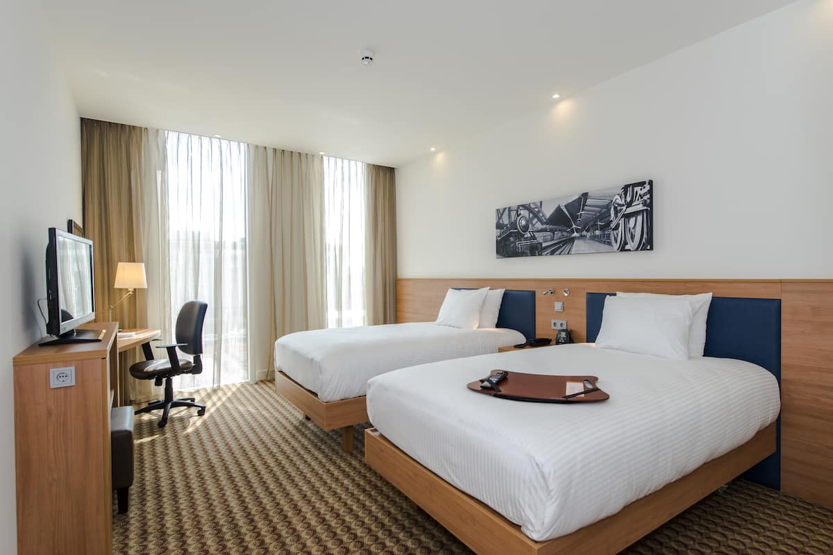 Ein Hotelzimmer mit zwei Betten, einem Schreibtisch mit Computer, einem Stuhl und einem Fernseher.