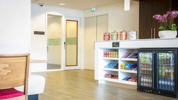 A hotel lobby with a reception area, a seating area, a snack bar, and a refrigerator stocked with beverages.