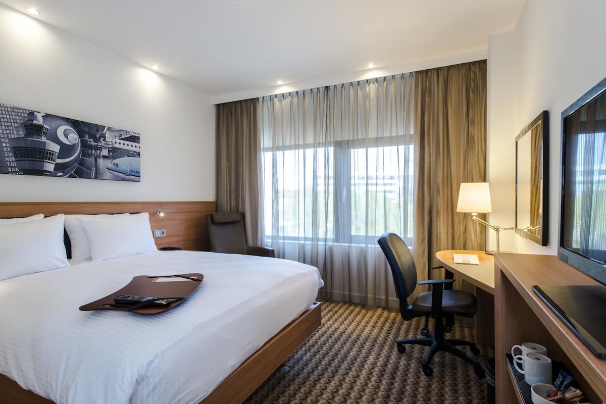Ein Hotelzimmer mit einem großen Bett, einem Schreibtisch mit Stuhl, einem Fernseher und einem Fenster mit Vorhängen.