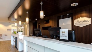 A modern hotel reception area with a white reception desk, multiple computer monitors, and a sign indicating 'Hilton Honors'. - Hampton by Hilton Amsterdam / Arena Boulevard (Amsterdam)