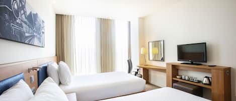 A hotel room with two beds, a desk with a television, and a painting on the wall.