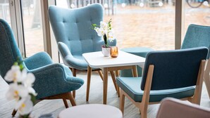 A seating area with teal chairs, a white table, and a potted orchid. - Hampton by Hilton Amsterdam / Arena Boulevard (Amsterdam)