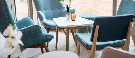 A seating area with teal chairs, a white table, and a potted orchid.