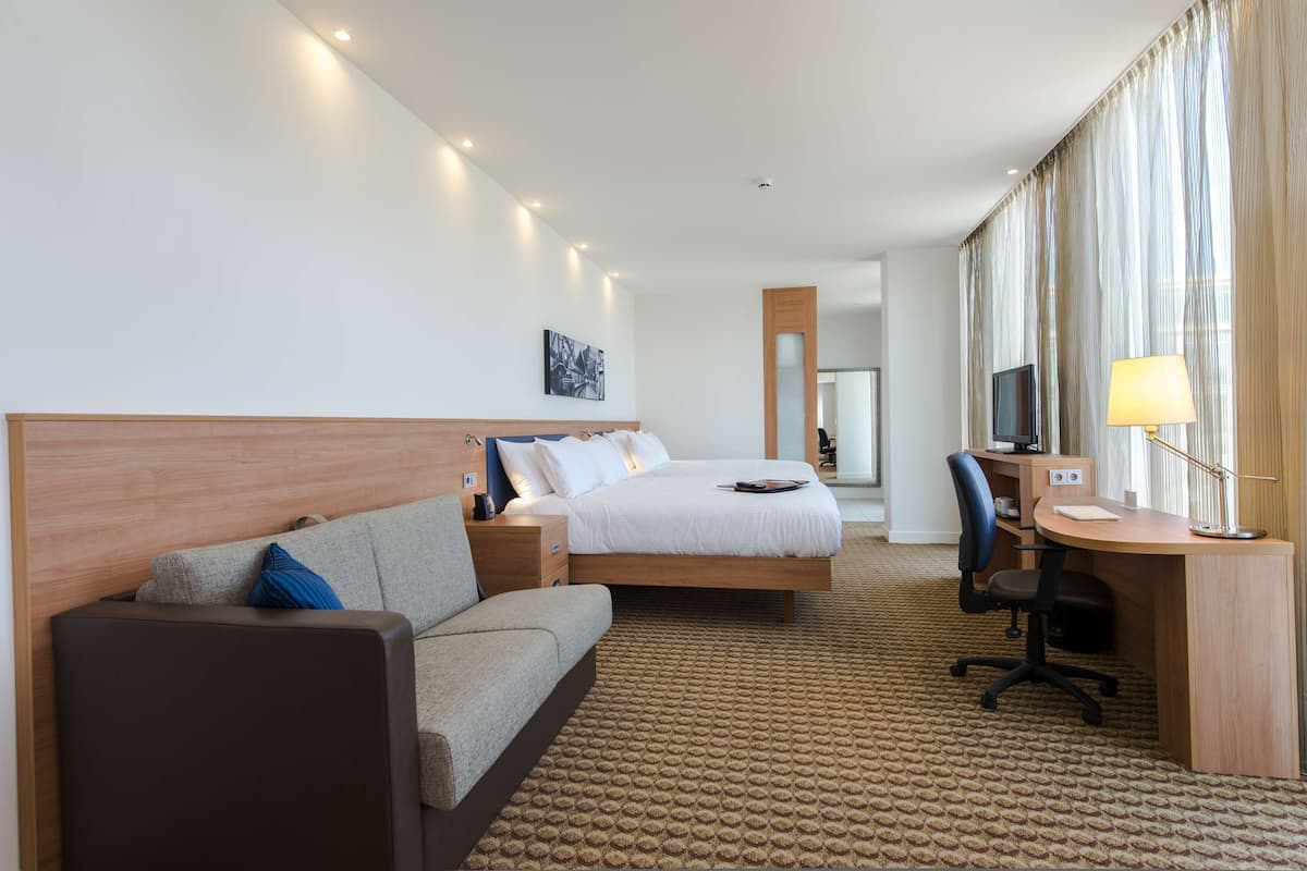 Ein Hotelzimmer mit einem Bett, einem Schreibtisch, einem Sessel, einer Couch und einem Fernseher.