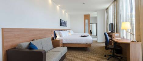 A hotel room with a bed, a desk, a chair, a sofa, and a television.