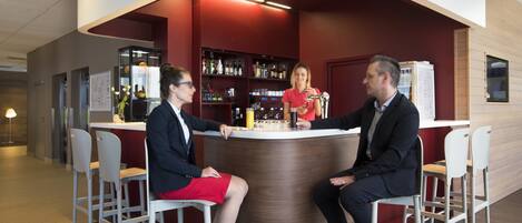 A modern bar area with a curved counter, white bar stools, and a red accent wall.