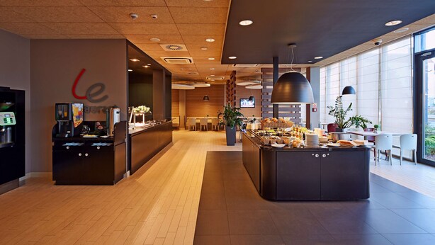 Un lobby moderno de hotel con un mostrador de recepción, una zona de buffet y arreglos de asientos.