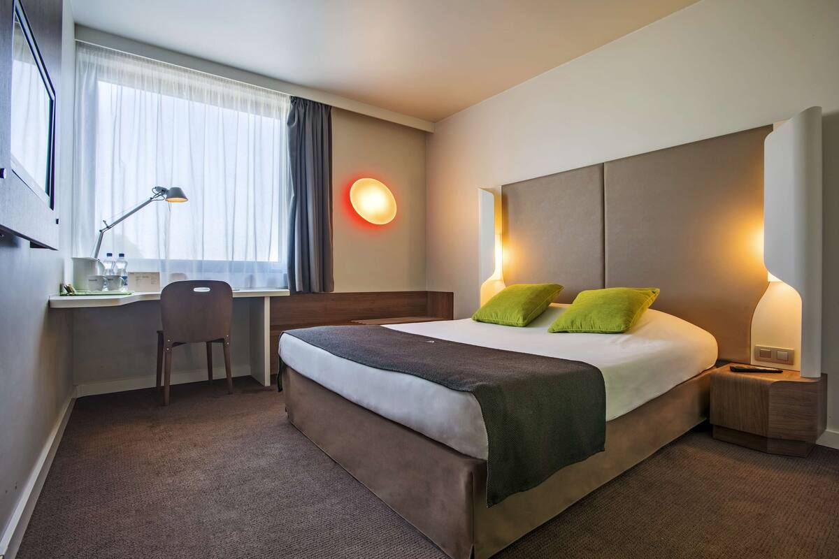 A hotel room with a bed, desk, chair, and bedside lamps.