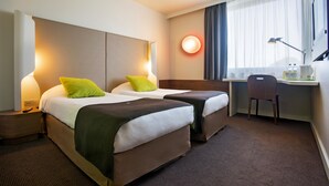 Habitación de hotel con dos camas, un escritorio, una silla y un ventanal con cortinas.