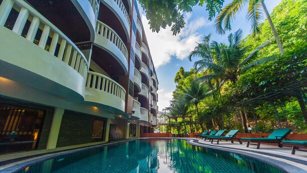 A swimming pool with a tiled floor, surrounded by lounge chairs and palm trees.