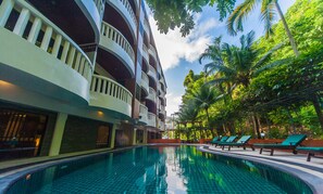 A swimming pool with a tiled floor, surrounded by lounge chairs and palm trees. - Ratana Hill Patong (Patong)