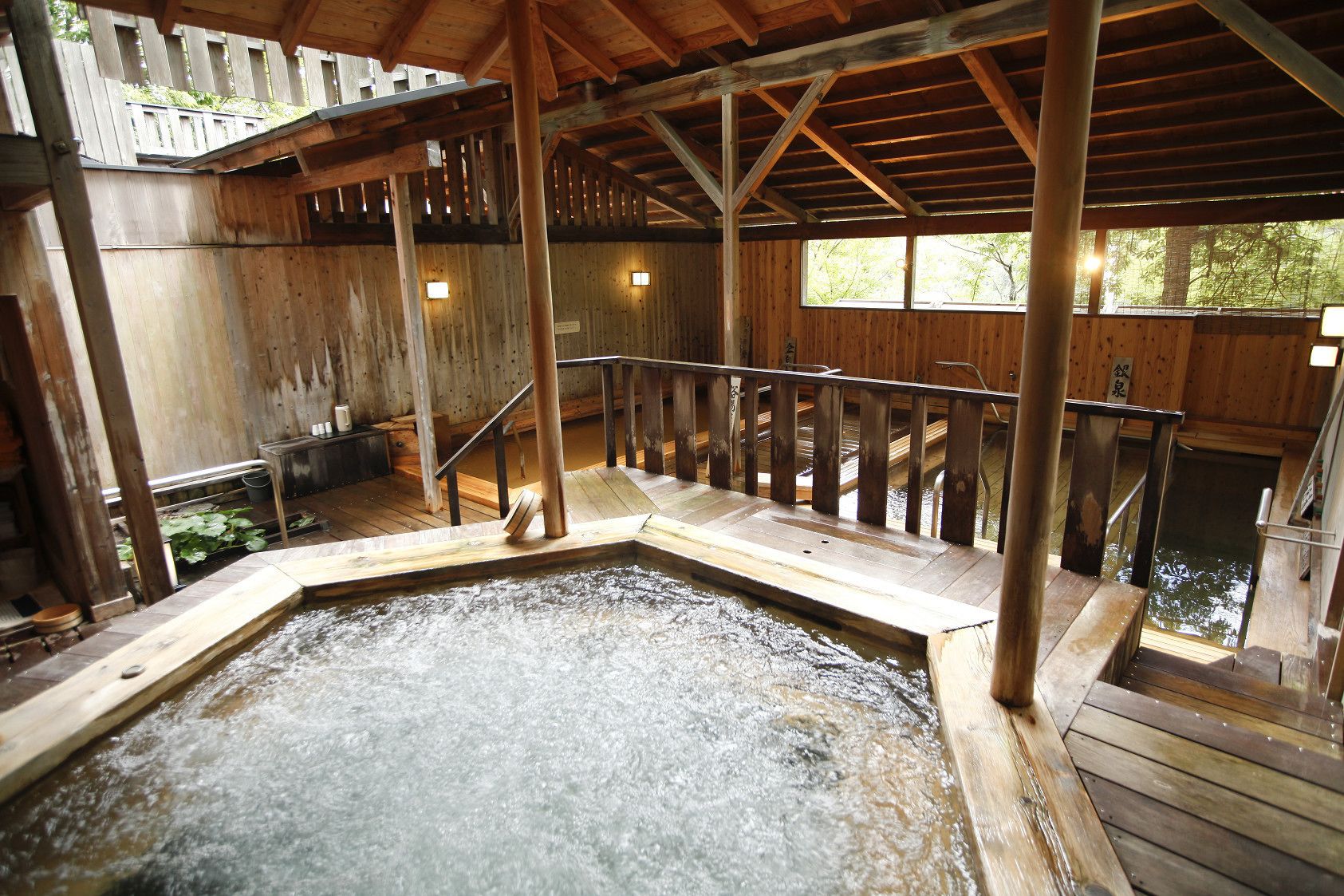 A wooden hot spring bath area with a wooden deck and railings, surrounded by wooden walls and a wooden ceiling.
