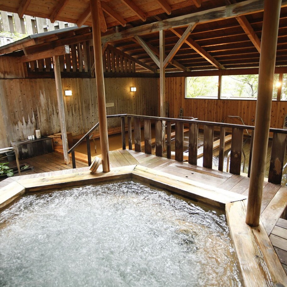 A wooden hot spring bath area with a wooden deck and railings, surrounded by wooden walls and a wooden ceiling.