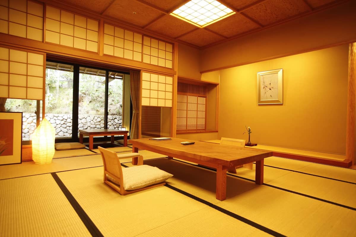 Una habitació japonesa tradicional amb fons de tatami, una taula baixa, una cadira amb coixí i portes corredisses.