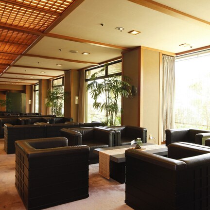 A spacious indoor area with multiple seating arrangements, large windows, and a ceiling with a grid-like pattern.