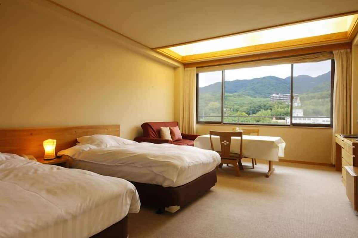 A hotel room with two beds, a desk, a chair, and a large window with a view of mountains.