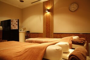 Une chambre d’hôtel avec deux lits, une horloge, une lampe fixée au mur et un mini-bar.
