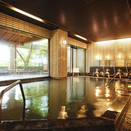 A traditional Japanese onsen with a wooden interior, a large window overlooking a natural setting, and a row of wooden benches.
