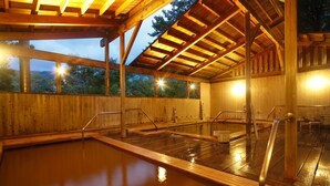 A wooden spa with a hot tub, wooden beams, and a view of trees outside.