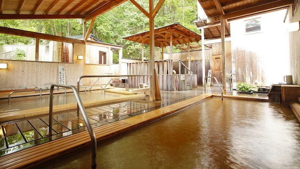 A traditional wooden bathhouse with multiple hot spring baths, wooden railings, and a covered seating area.