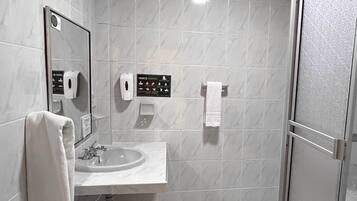A bathroom with a sink, mirror, hand soap dispenser, and a towel rack.