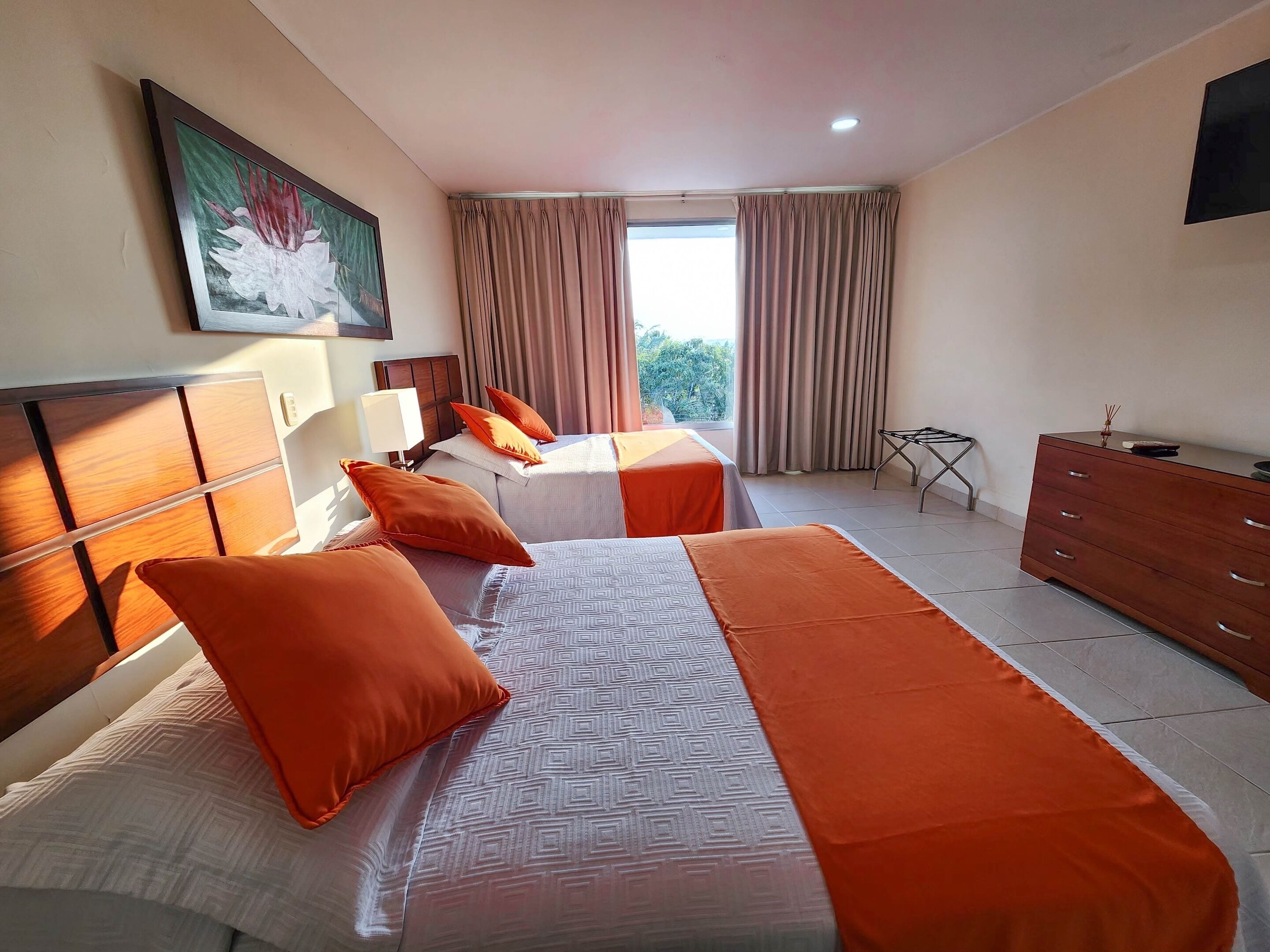 A hotel room with two beds, a wooden dresser, a small table, and a painting on the wall.