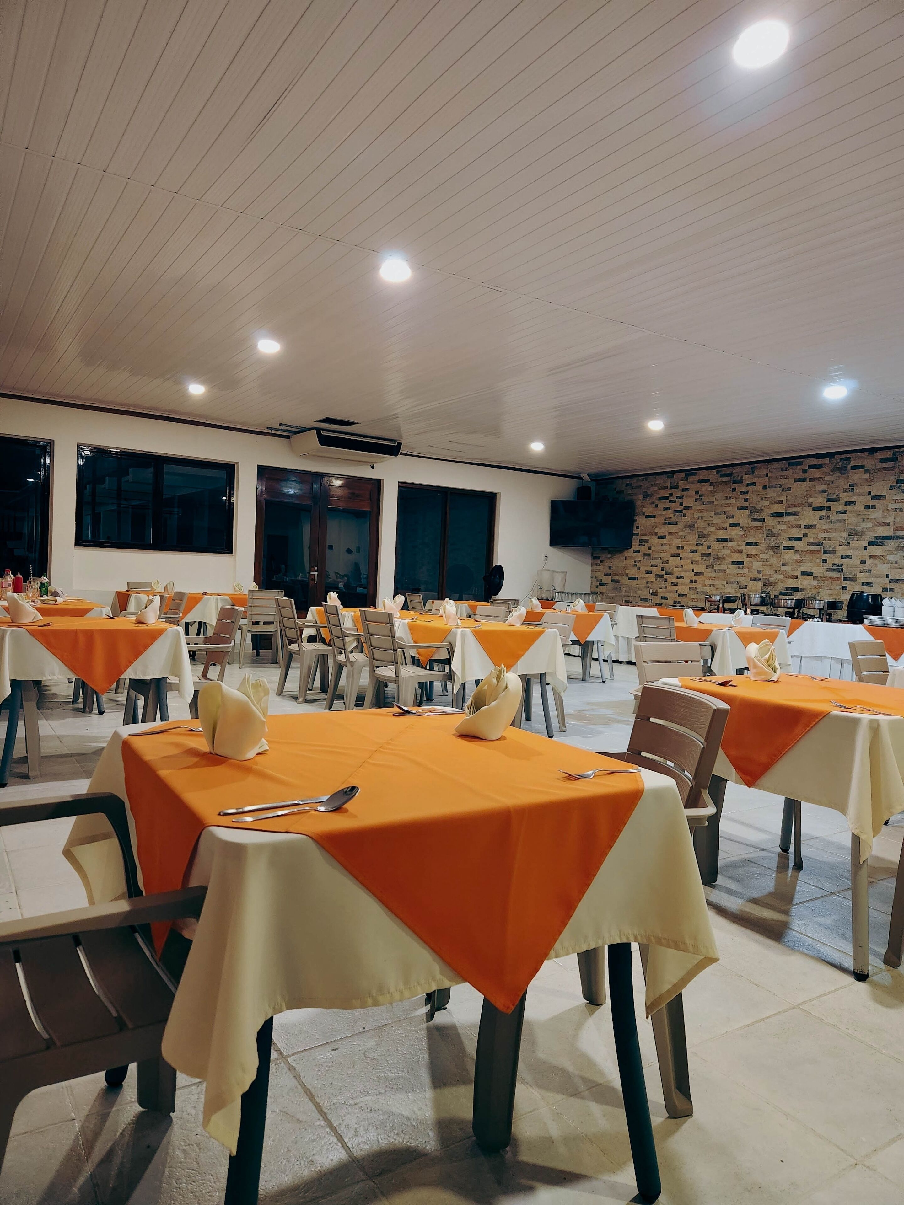A spacious indoor dining area with multiple tables set for guests, featuring a high ceiling and large windows.