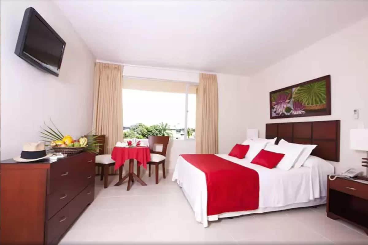 A hotel room with a bed, a desk, a chair, a TV, and a window with curtains.