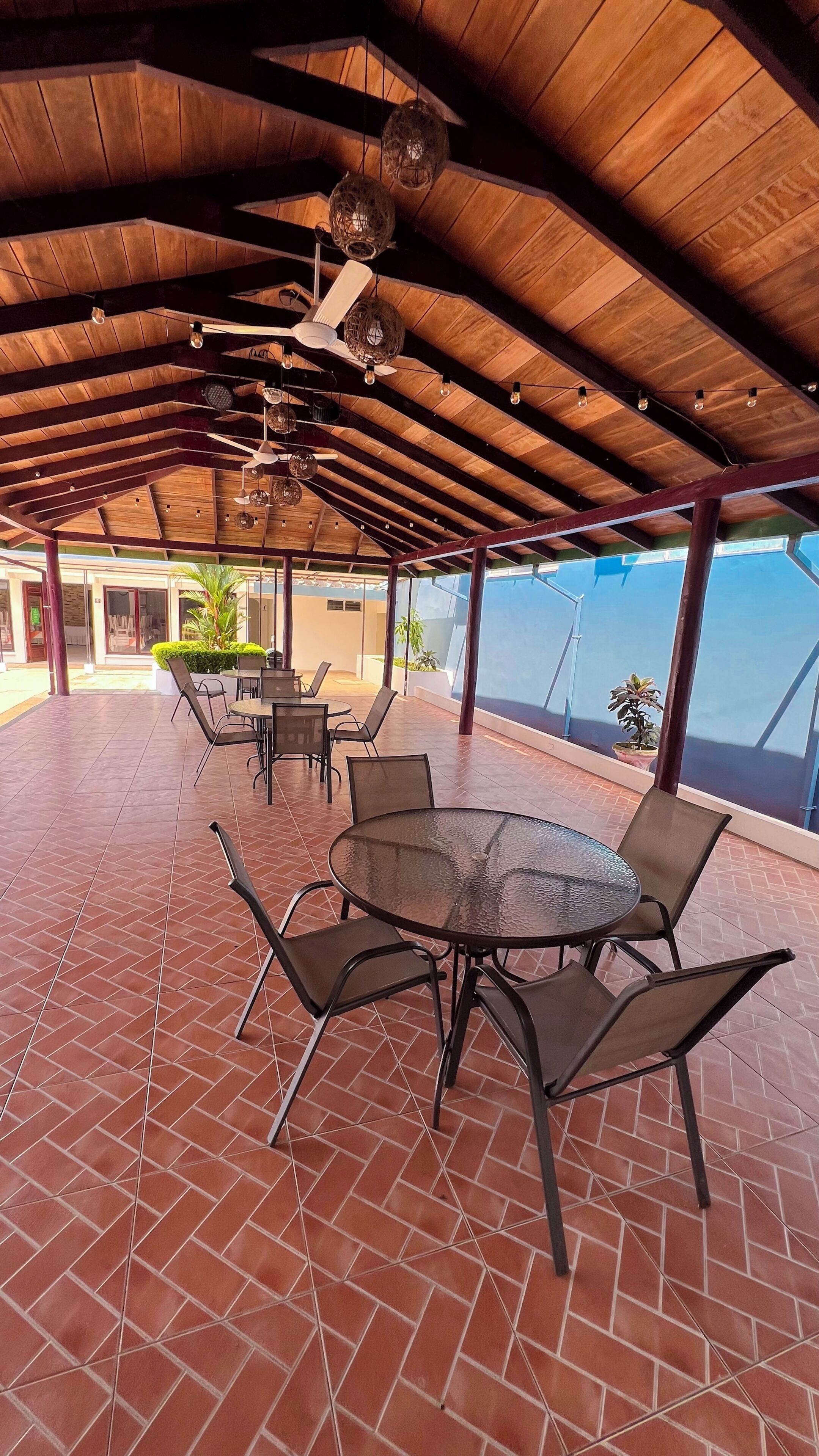 An outdoor patio with tiled flooring, round tables with chairs, and hanging light fixtures.