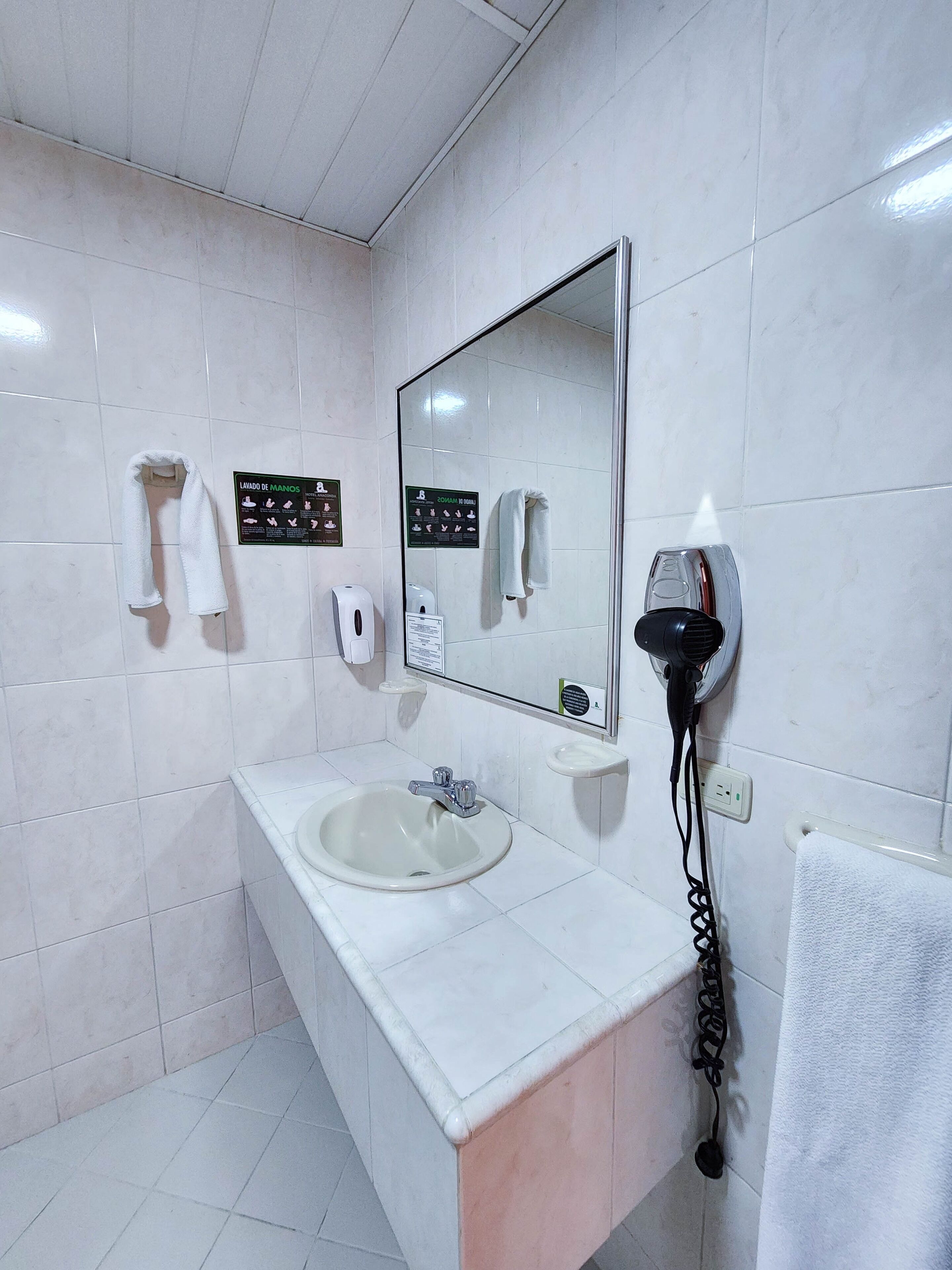 A bathroom with a sink, mirror, towel rack, hand dryer, and a hairdryer.