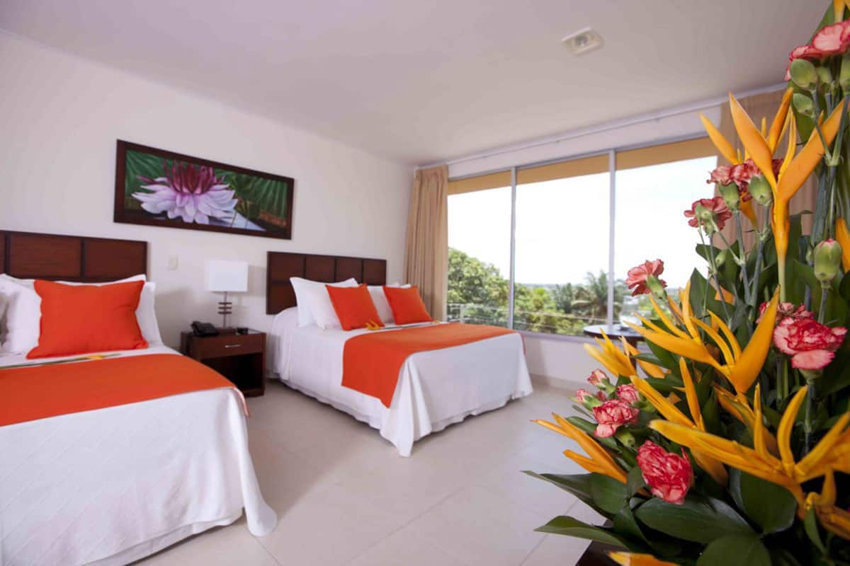 A hotel room with two beds, a large window, and a tropical flower arrangement.