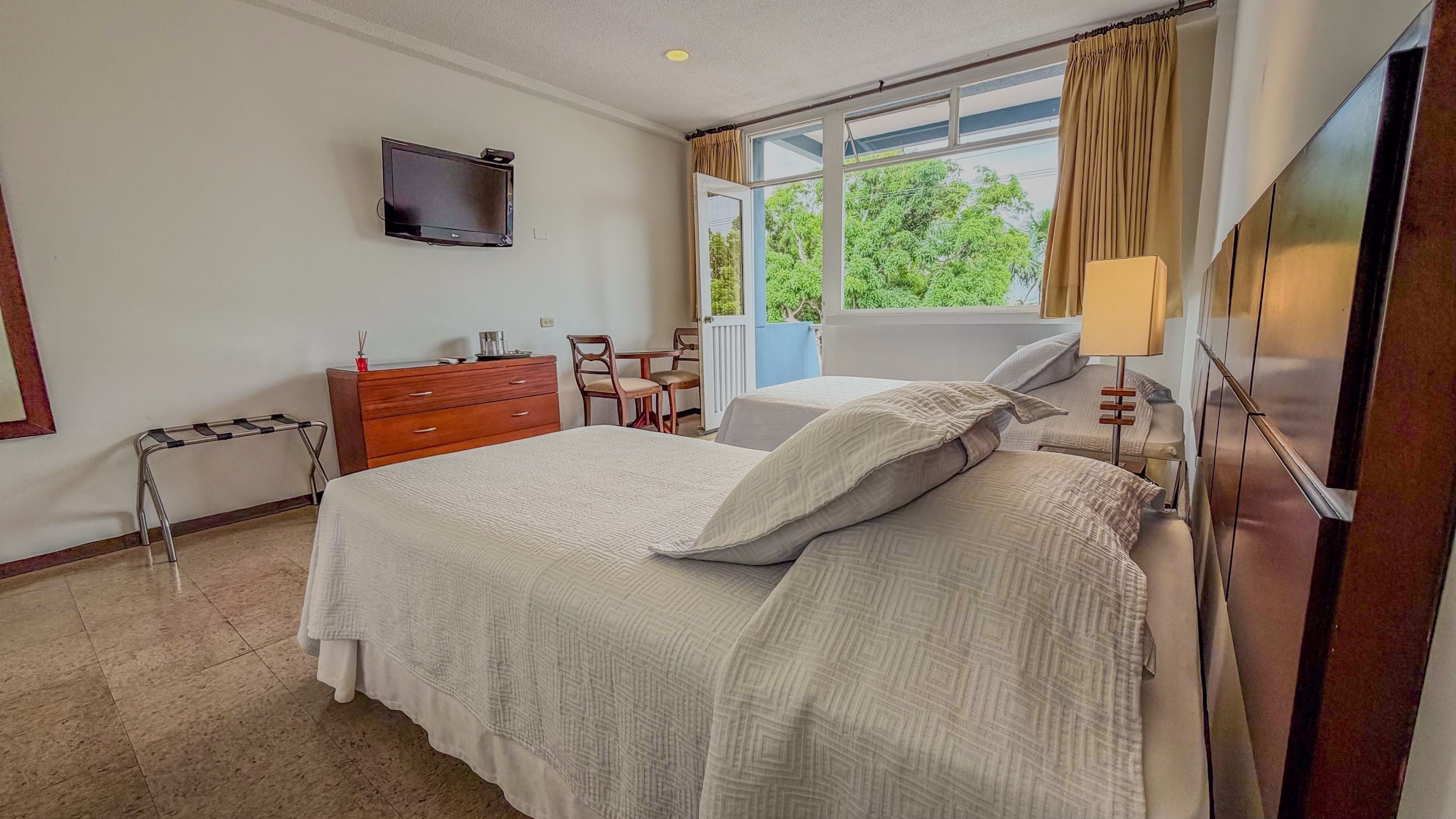 Une chambre d’hôtel avec un lit, un bureau, une chaise, une télévision et une fenêtre avec des rideaux.
