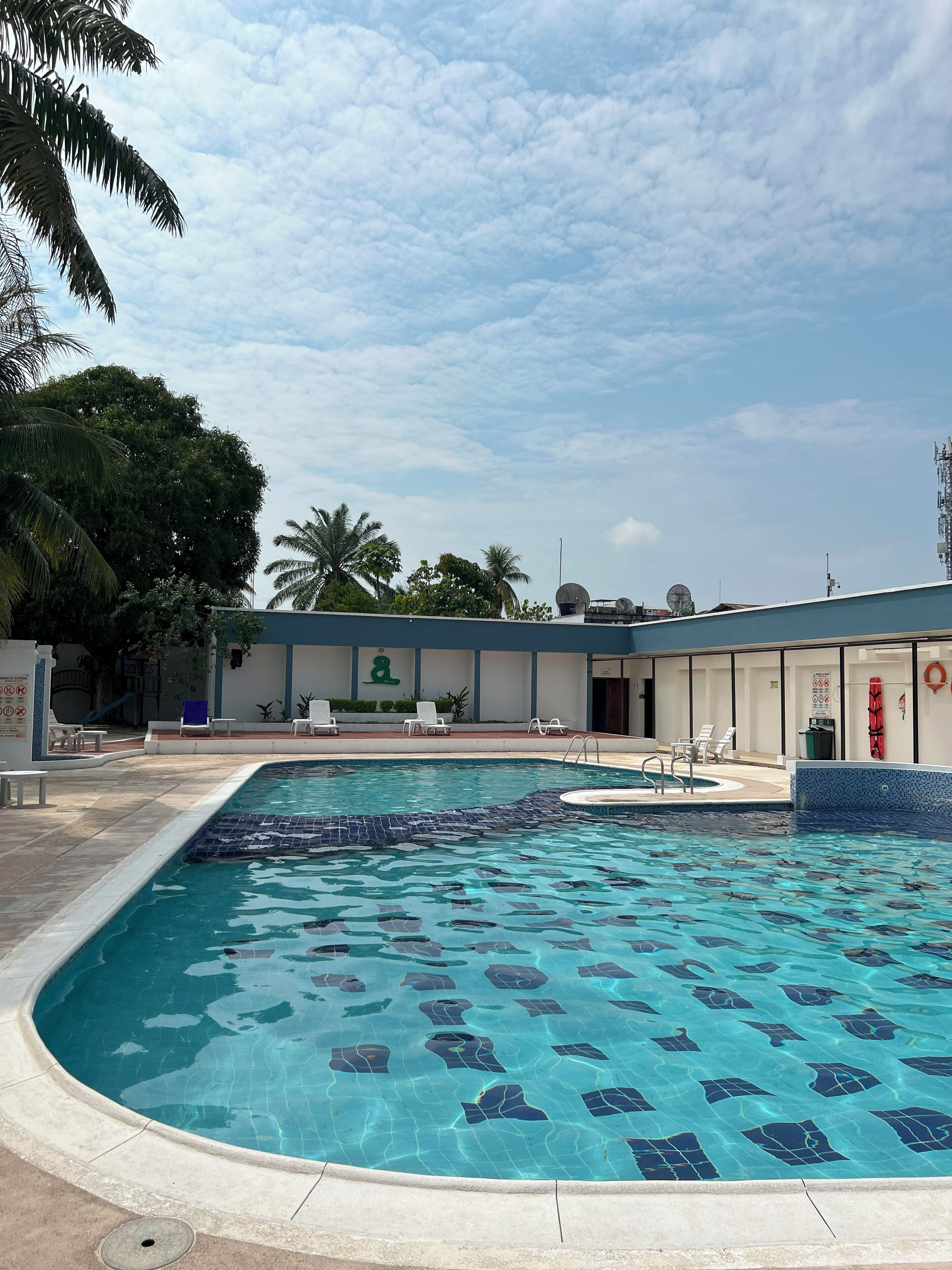Una piscina con agua azul cristalina, rodeada de sillas de descanso y palmeras.