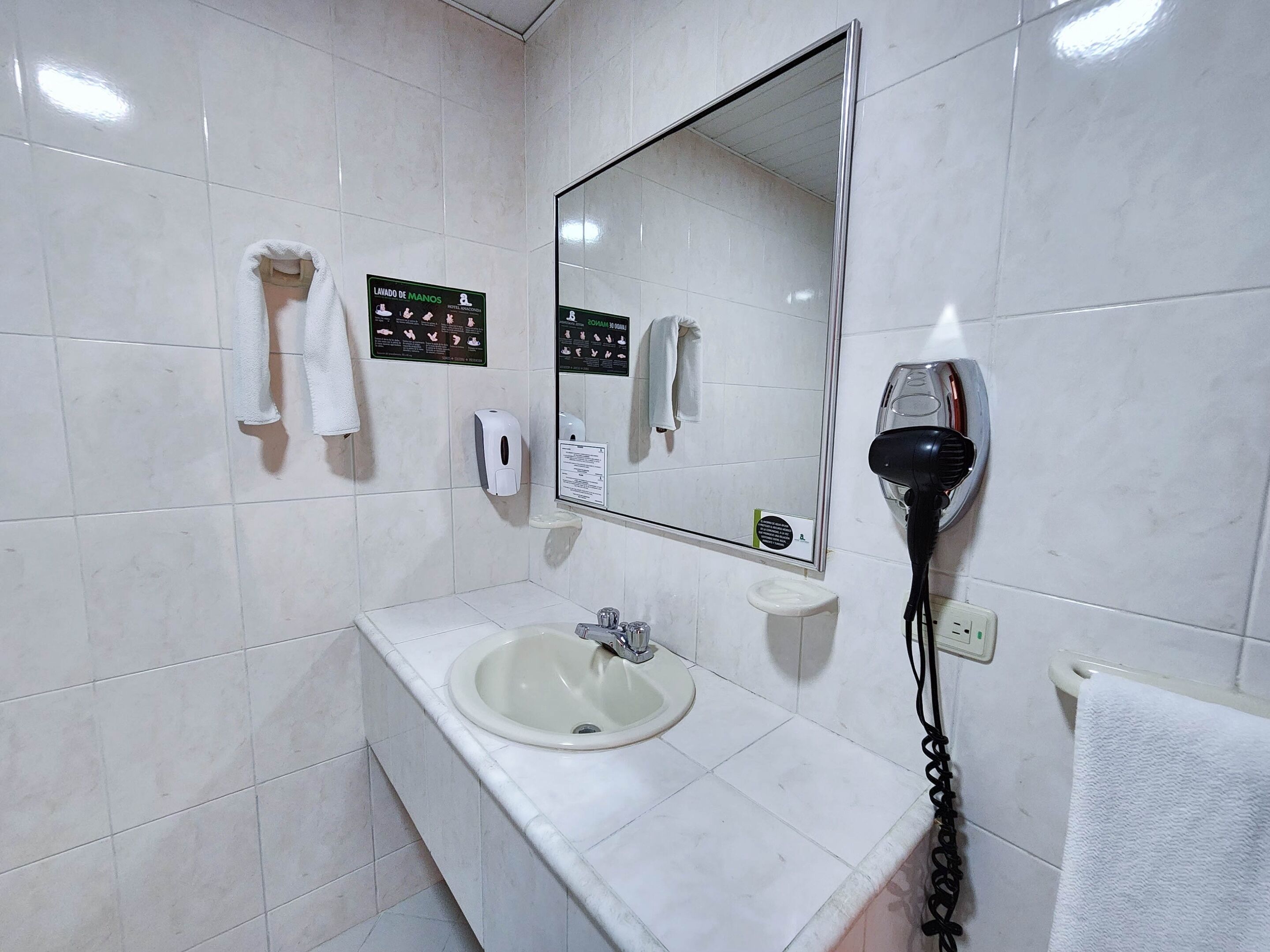 A bathroom with a sink, mirror, hand dryer, and towel rack.