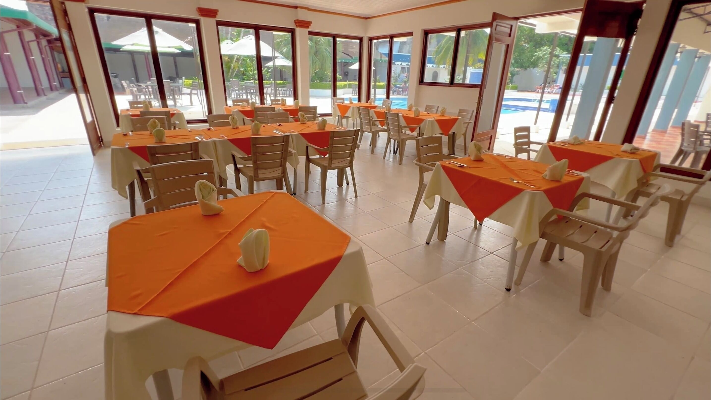 A dining area with tables set for service, large windows, and a view of the outdoor pool area.