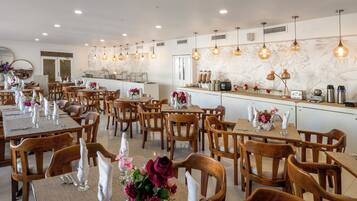 Un restaurante con mesas y sillas de madera, servilletas blancas y centros de mesa con flores.