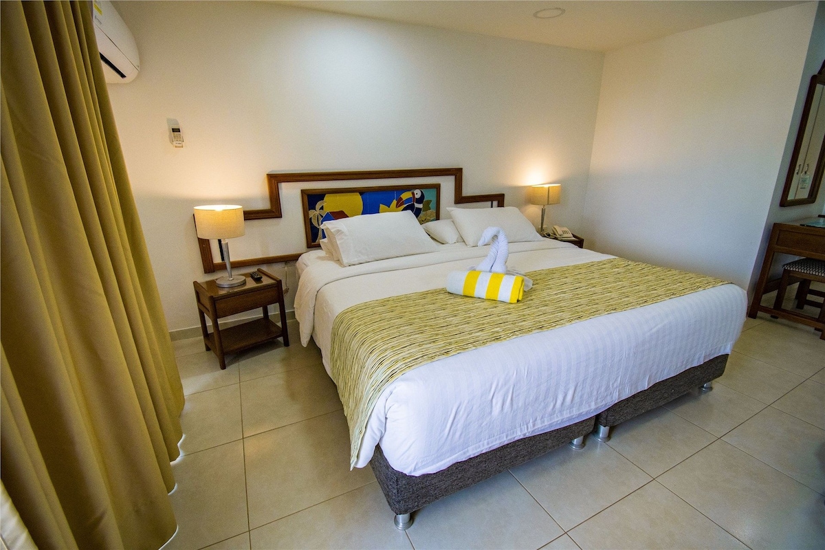 Habitación de hotel con una cama, dos mesitas de noche, una lámpara, un teléfono y un cuadro en la pared.