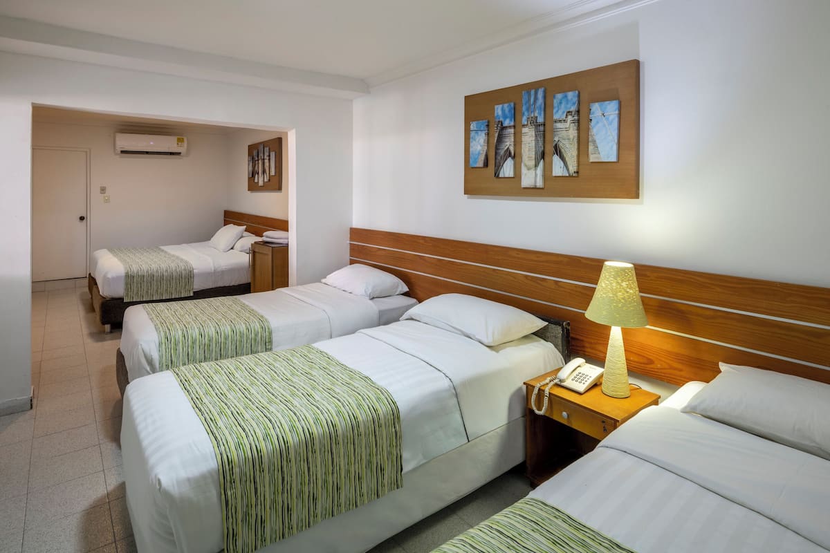A hotel room with two beds, a wooden headboard, a bedside lamp, a telephone, and a wall-mounted air conditioner.